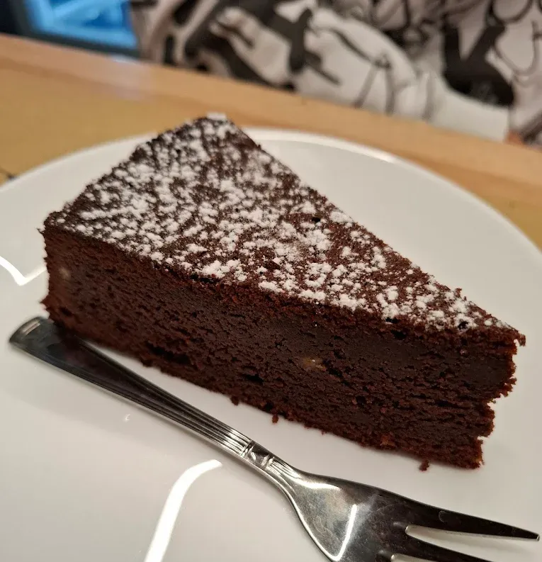 Fetta di torta al cioccolato fondente spolverata con zucchero a velo su un piatto bianco con una forchetta.