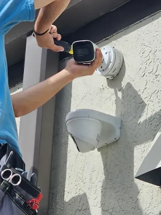 Person installs a security camera on a stucco wall.  A second camera is mounted below.
