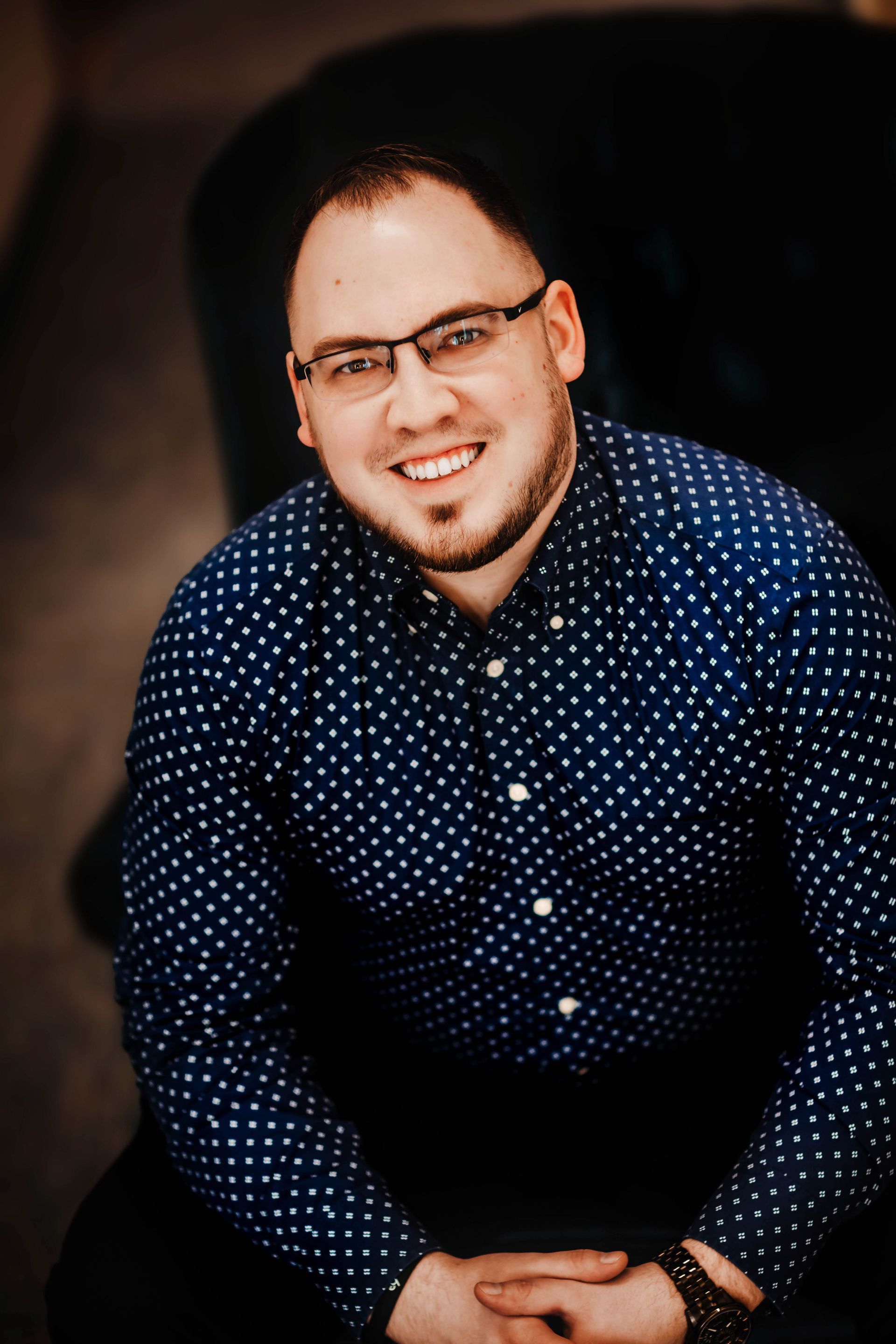 A man wearing glasses and a blue shirt is smiling for the camera.