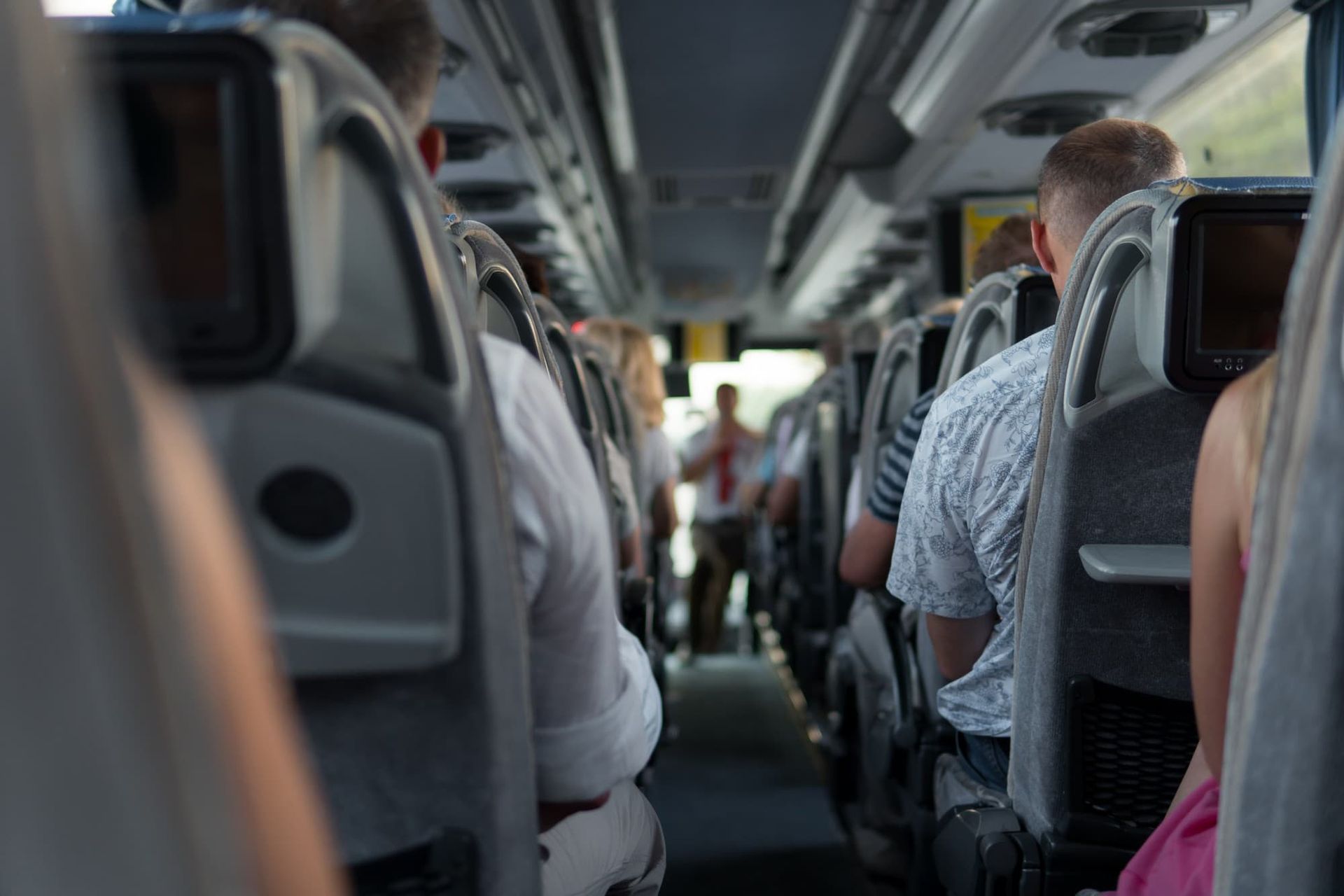 Vista interna de um ônibus com passageiros sentados. As pessoas são vistas de costas, olhando para a frente.