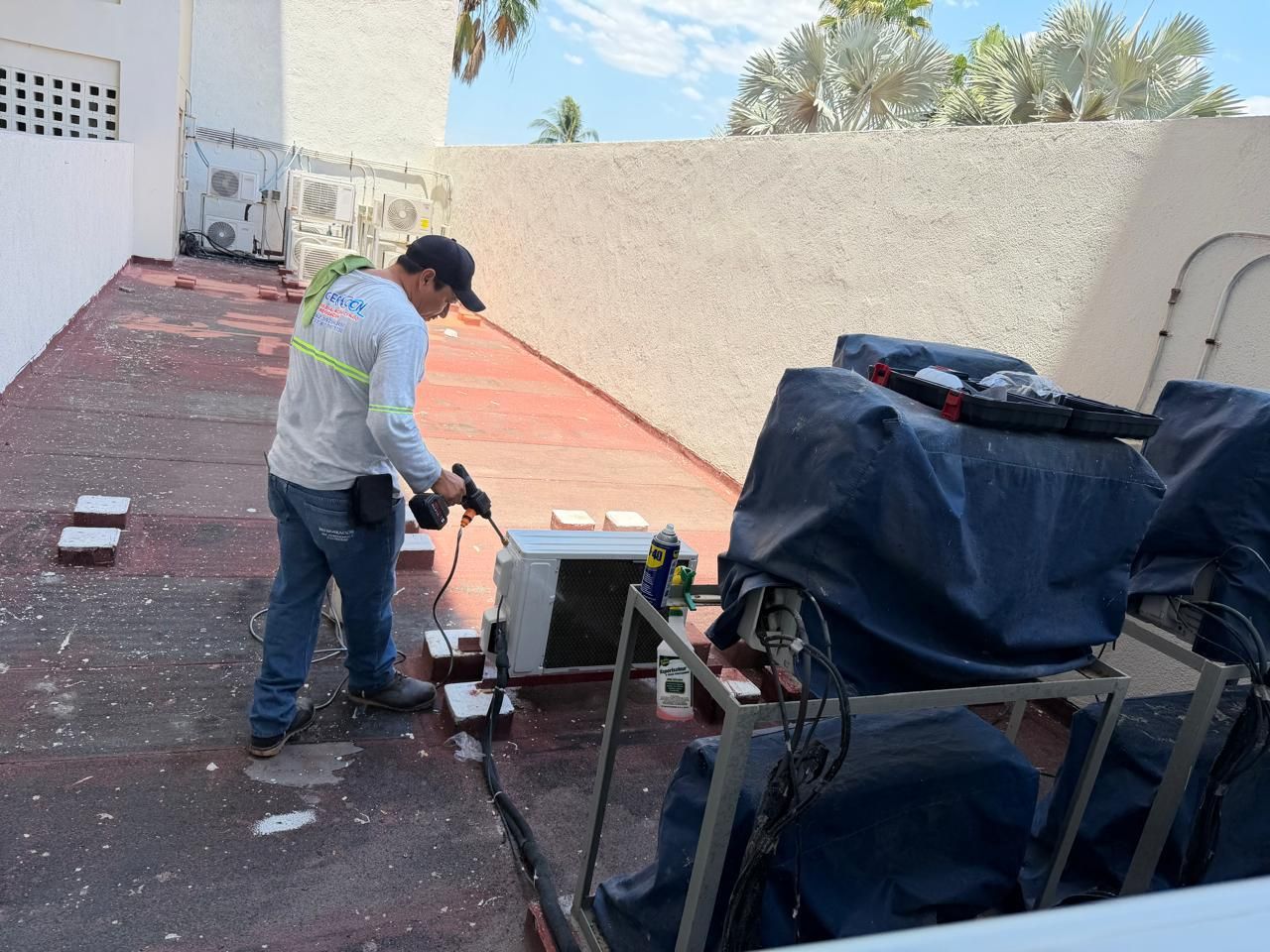 Un trabajador maneja una sierra en un patio de concreto rojo junto a una pared blanca, con el equipo cubierto cerca.
