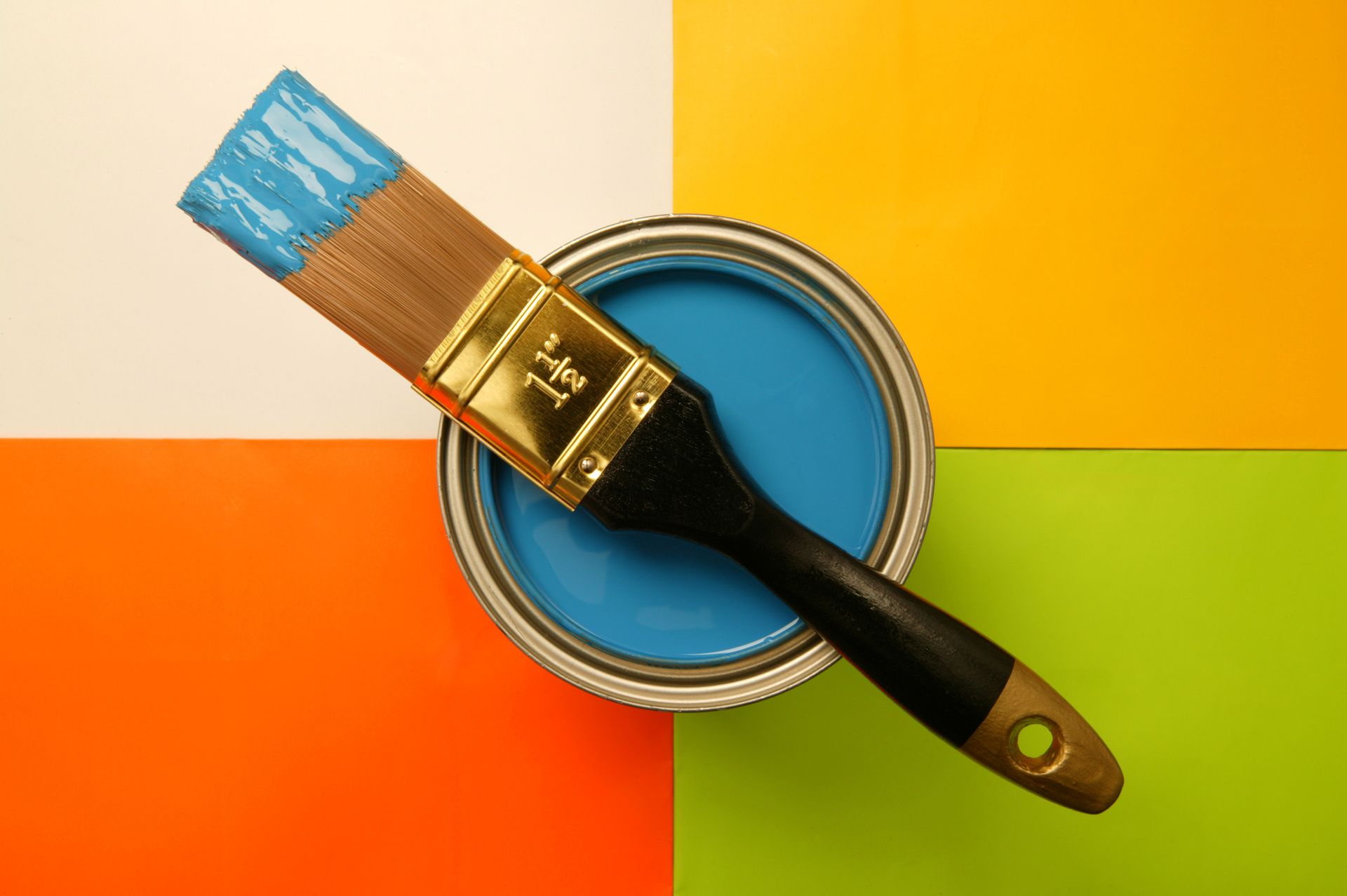 Paintbrush dipped in blue paint, resting on an open can against a background of white, orange, yellow, and green squares.