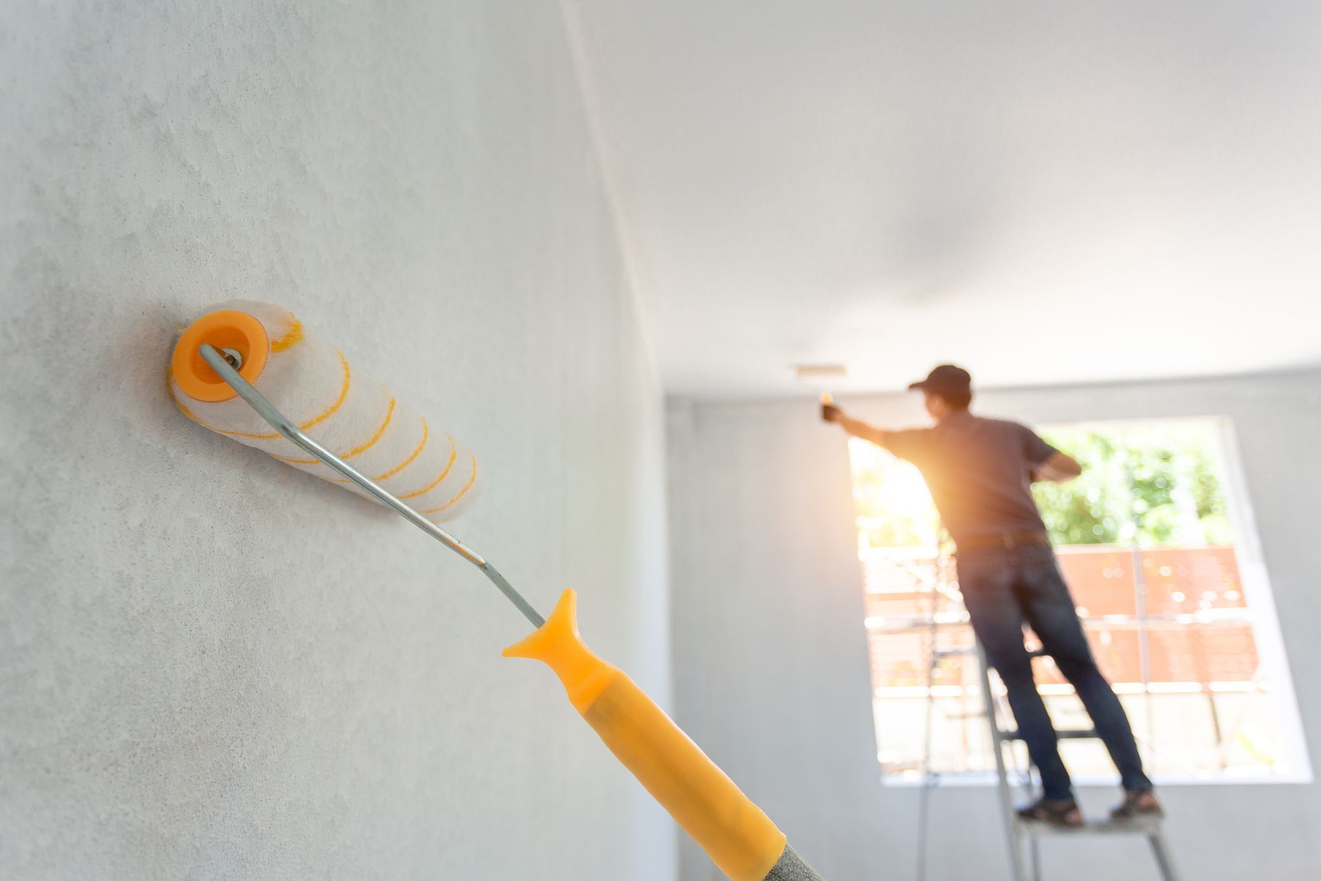Person painting a white wall with a paint roller; interior shot.