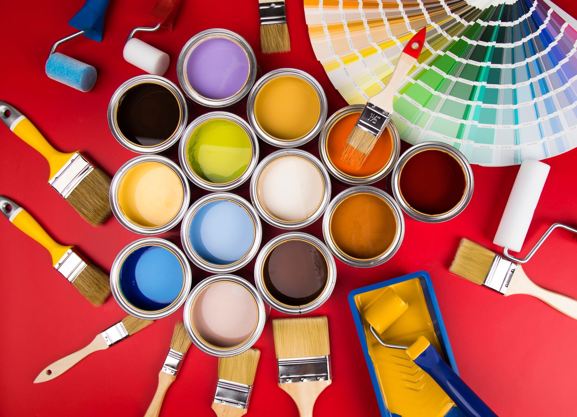 Paint cans in various colors with brushes and a color swatch against a red backdrop.