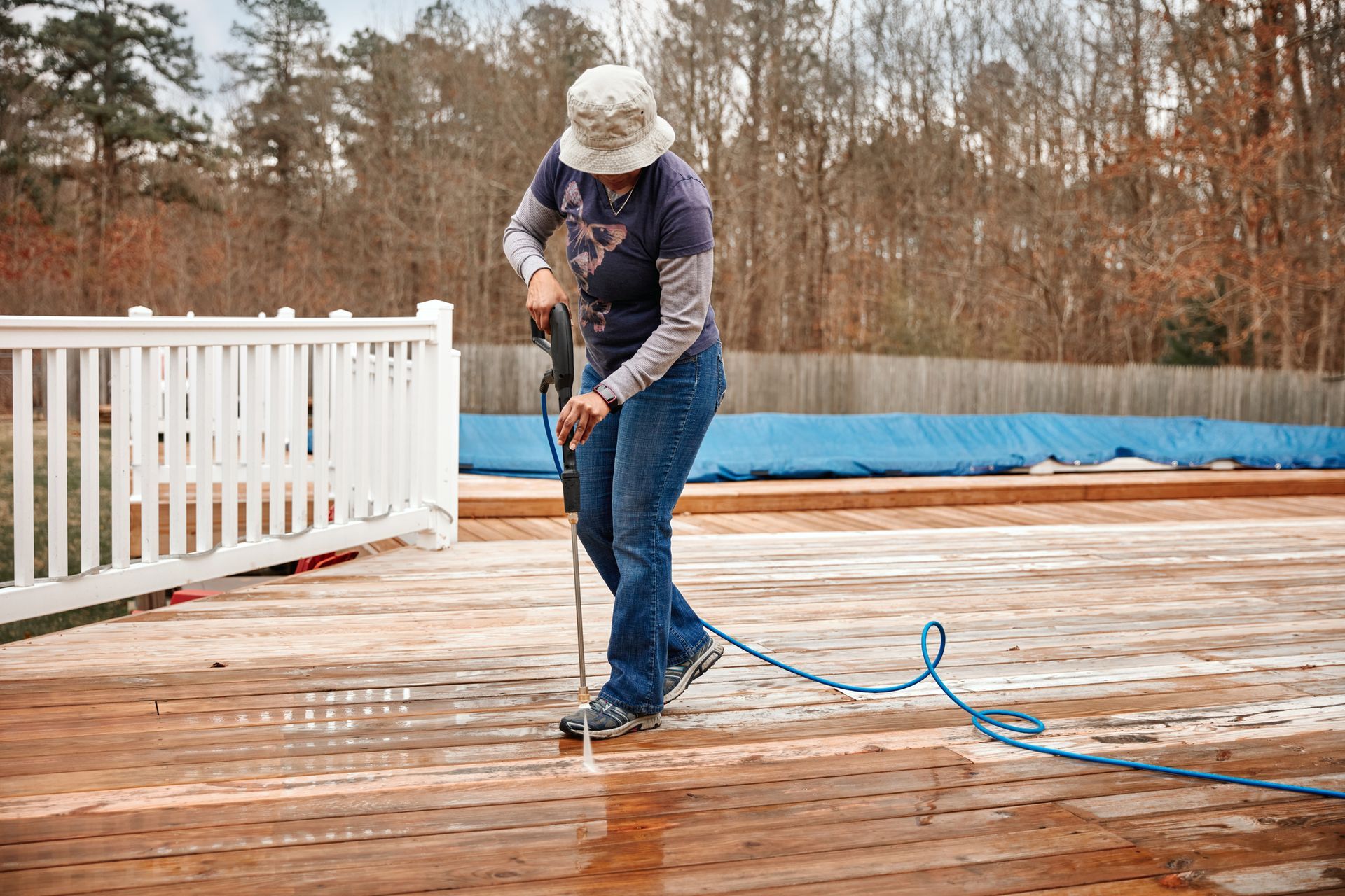 Person power washing a wooden deck outdoors.