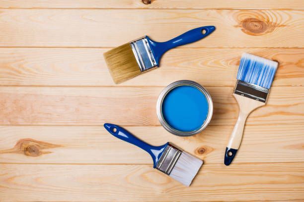 Paintbrushes and blue paint can on a wooden surface.