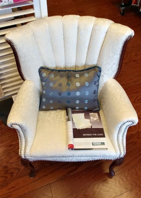 White upholstered armchair with patterned back, blue pillow, and fabric sample on seat.