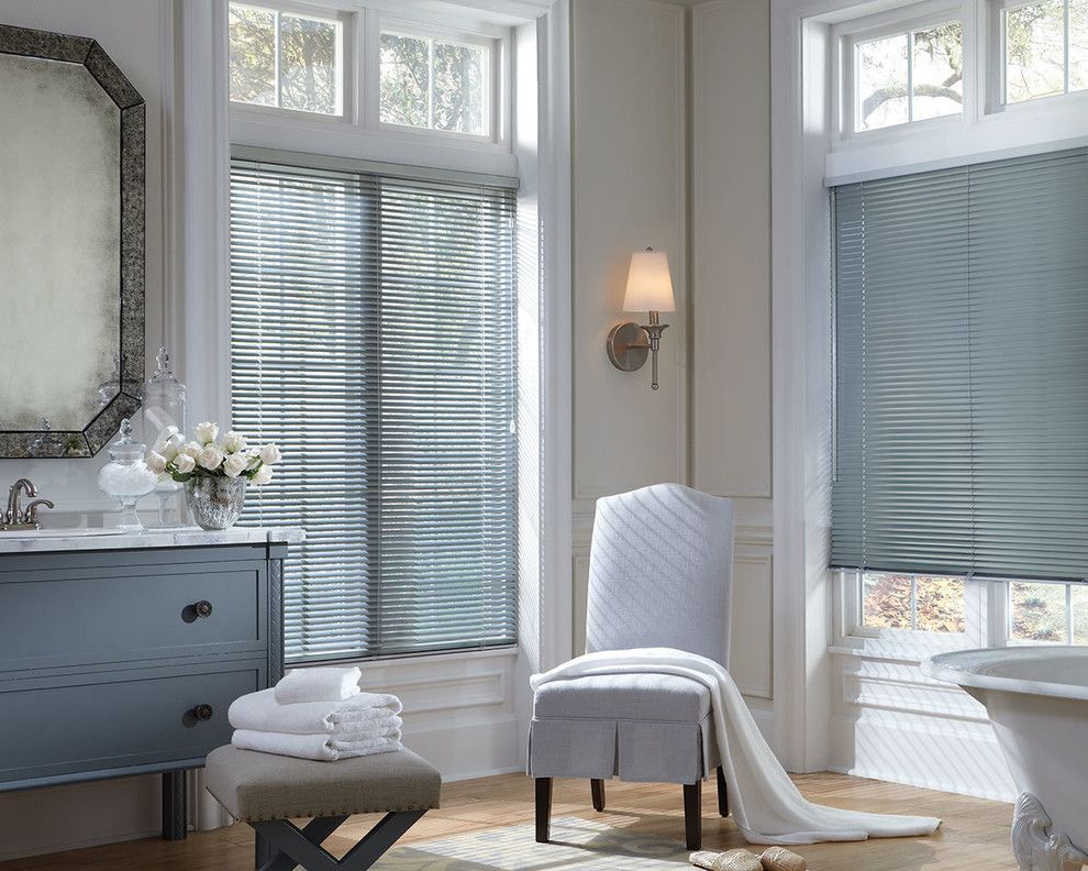 Bathroom with blue vanity, a chair with a white blanket, and windows with blue blinds.