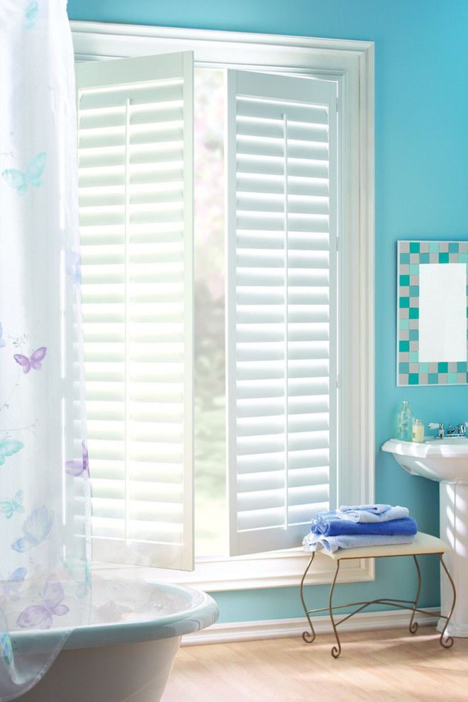 Bathroom with white shutters, tub, and sink; blue walls and accent mirror.