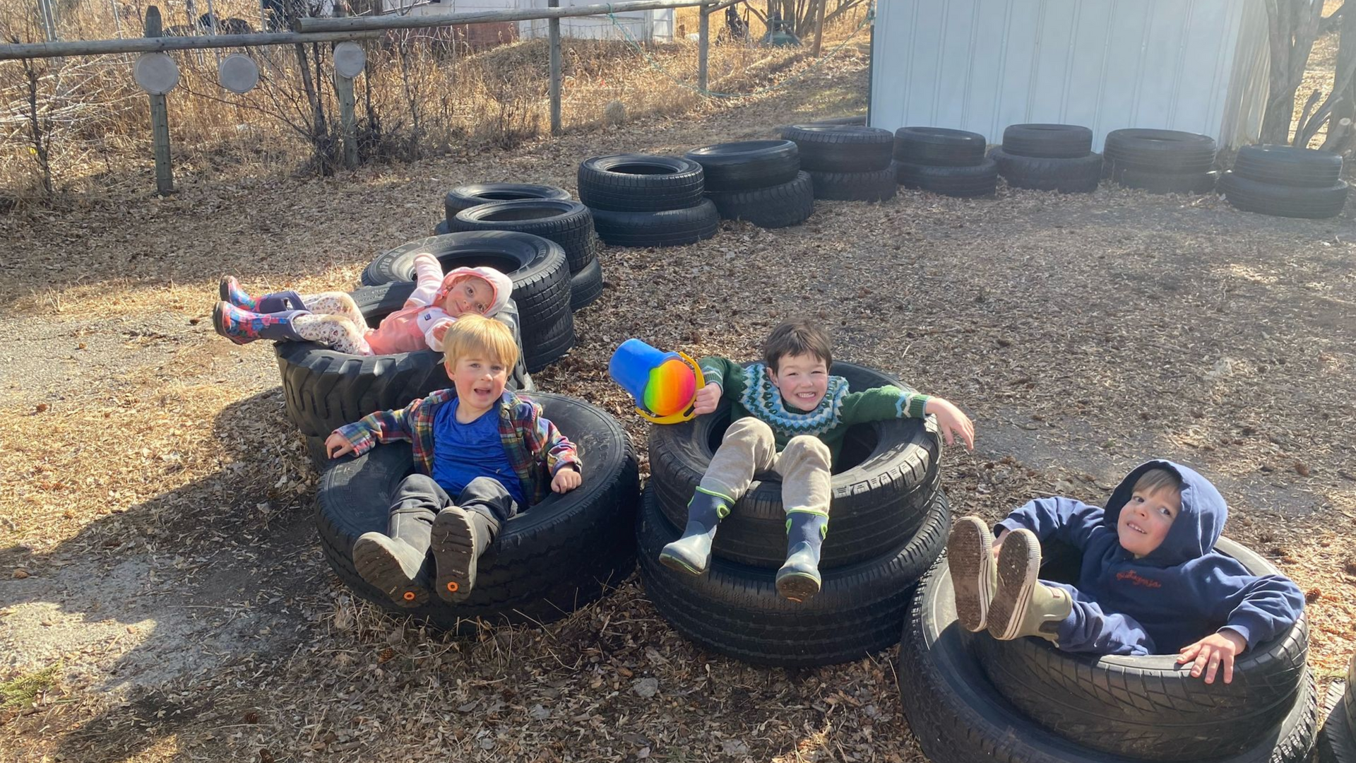 Four children smiling in a yellow inflatable pool outdoors on a sunny day