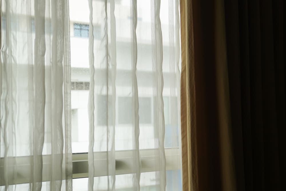 A Close Up Of A Window With White Curtains And A Building In The Background — Summerland Screens & Awnings In Suffolk Park, NSW