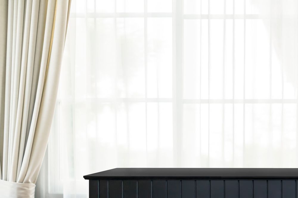 A Black Dresser Is Sitting In Front Of A Large Window With White Curtains — Summerland Screens & Awnings In Suffolk Park, NSW