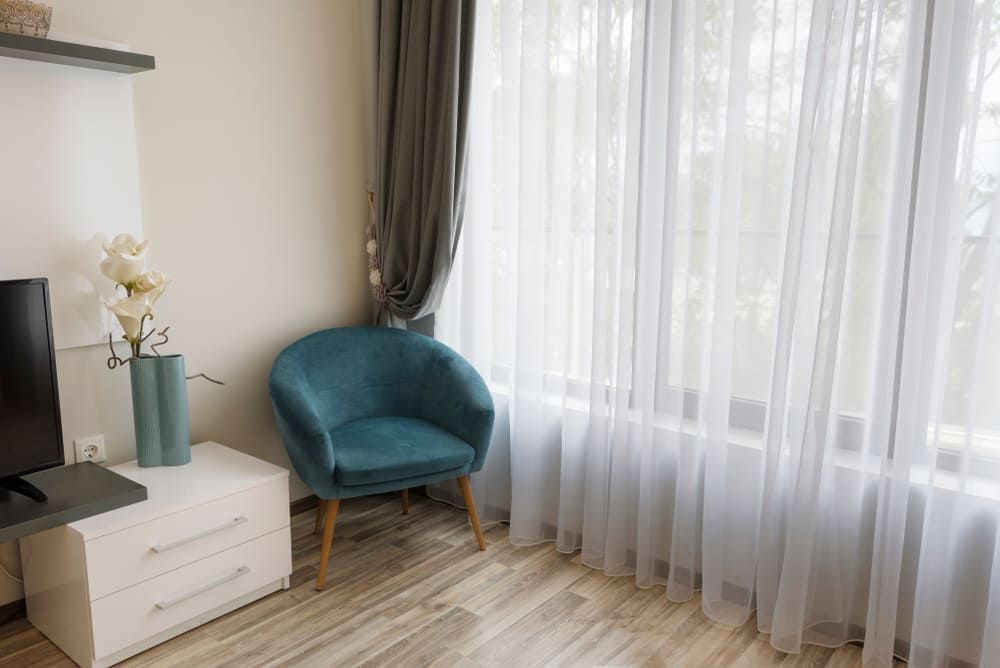 A Living Room With A Blue Chair, A Television, A Nightstand And A Window — Summerland Screens & Awnings In Lismore, NSW