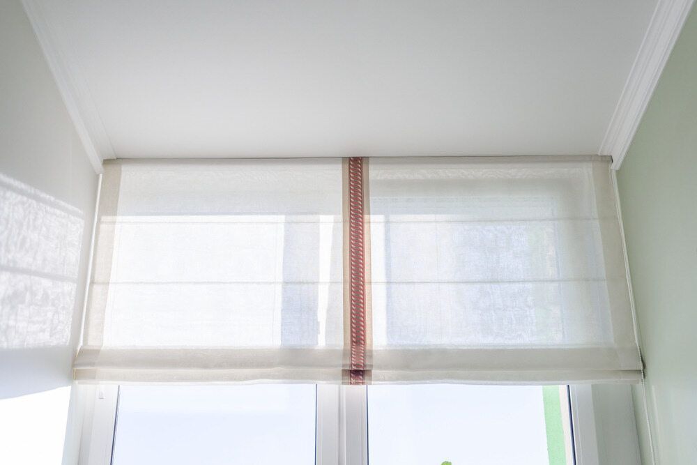 A White Roman Shade Is Hanging Over A Window In A Room — Summerland Screens & Awnings In Ballina, NSW