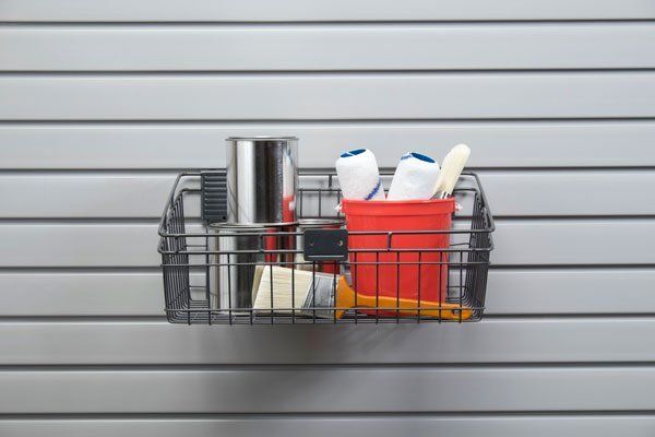 A wire basket filled with cleaning supplies is hanging on a wall.