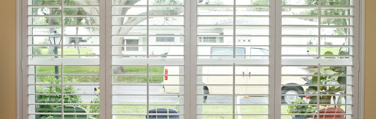 A window with shutters on it and a view of a yard.
