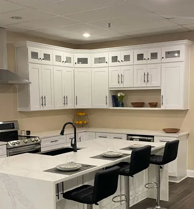 A kitchen with white cabinets , a stove , sink , and stools.
