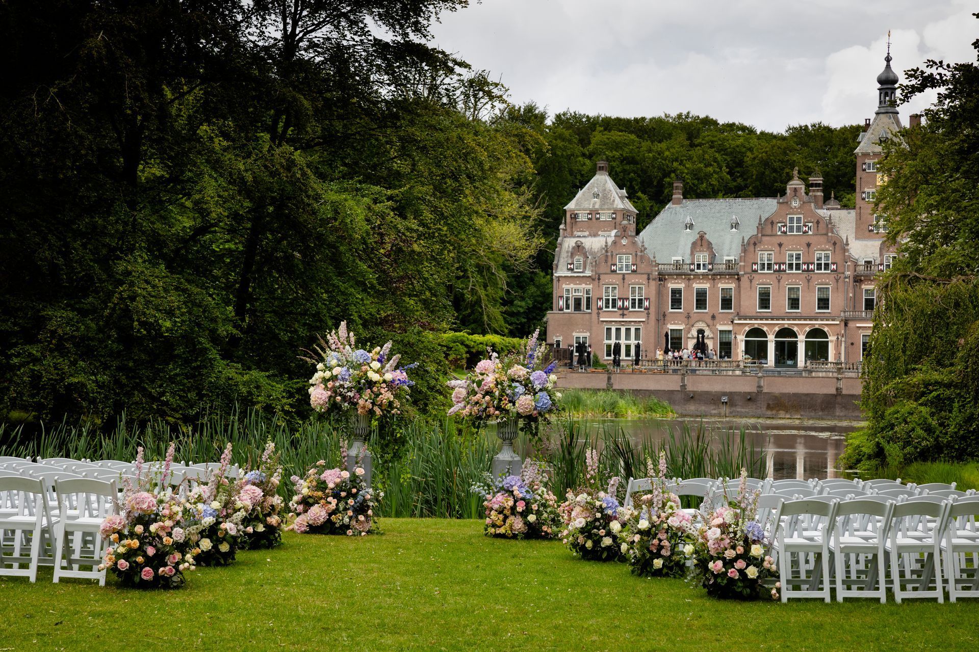Outdoor wedding setup with white chairs, floral arches, and a historic mansion in the background