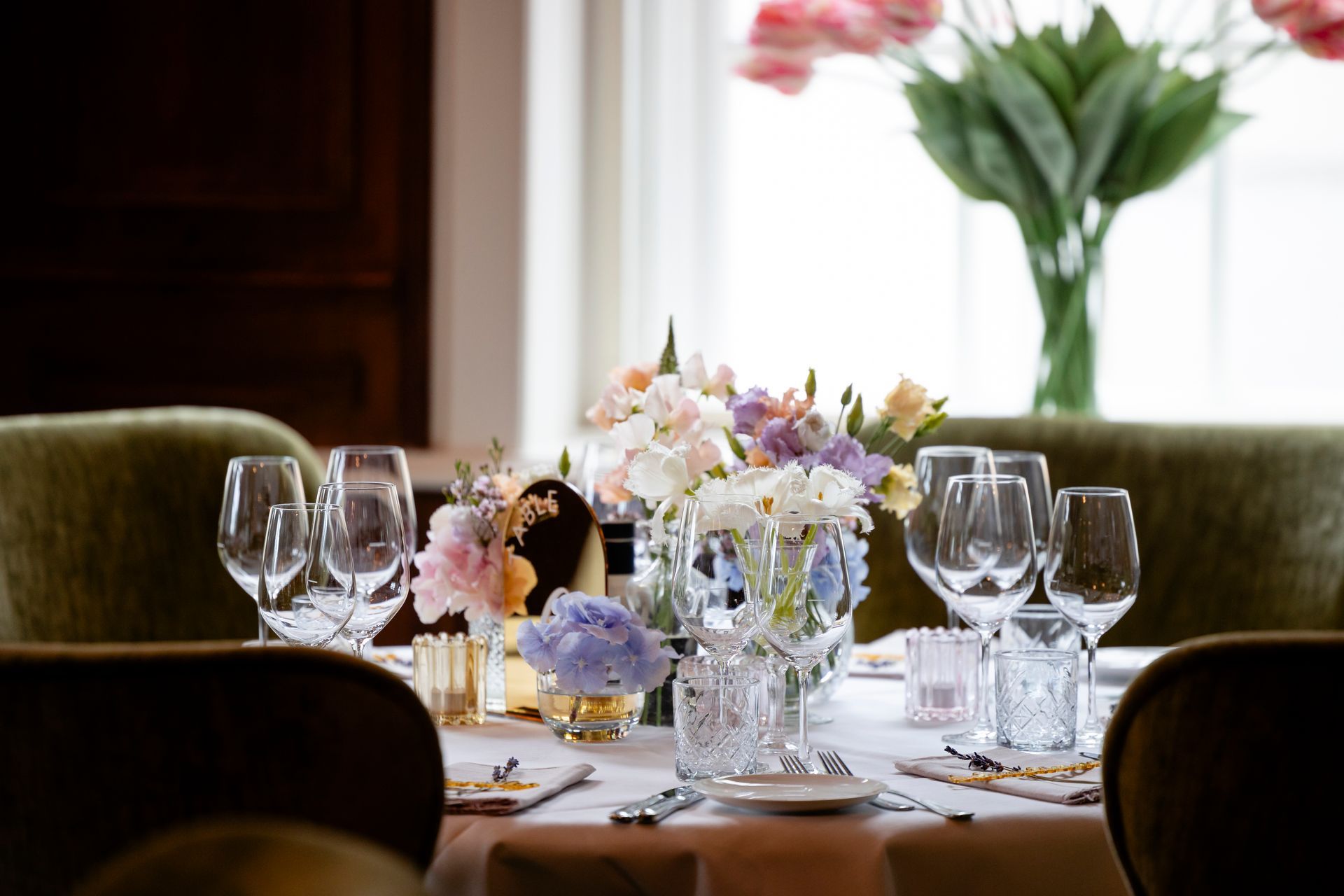 Elegant dining table set with floral centerpieces, wine glasses, and a softly lit window in the background