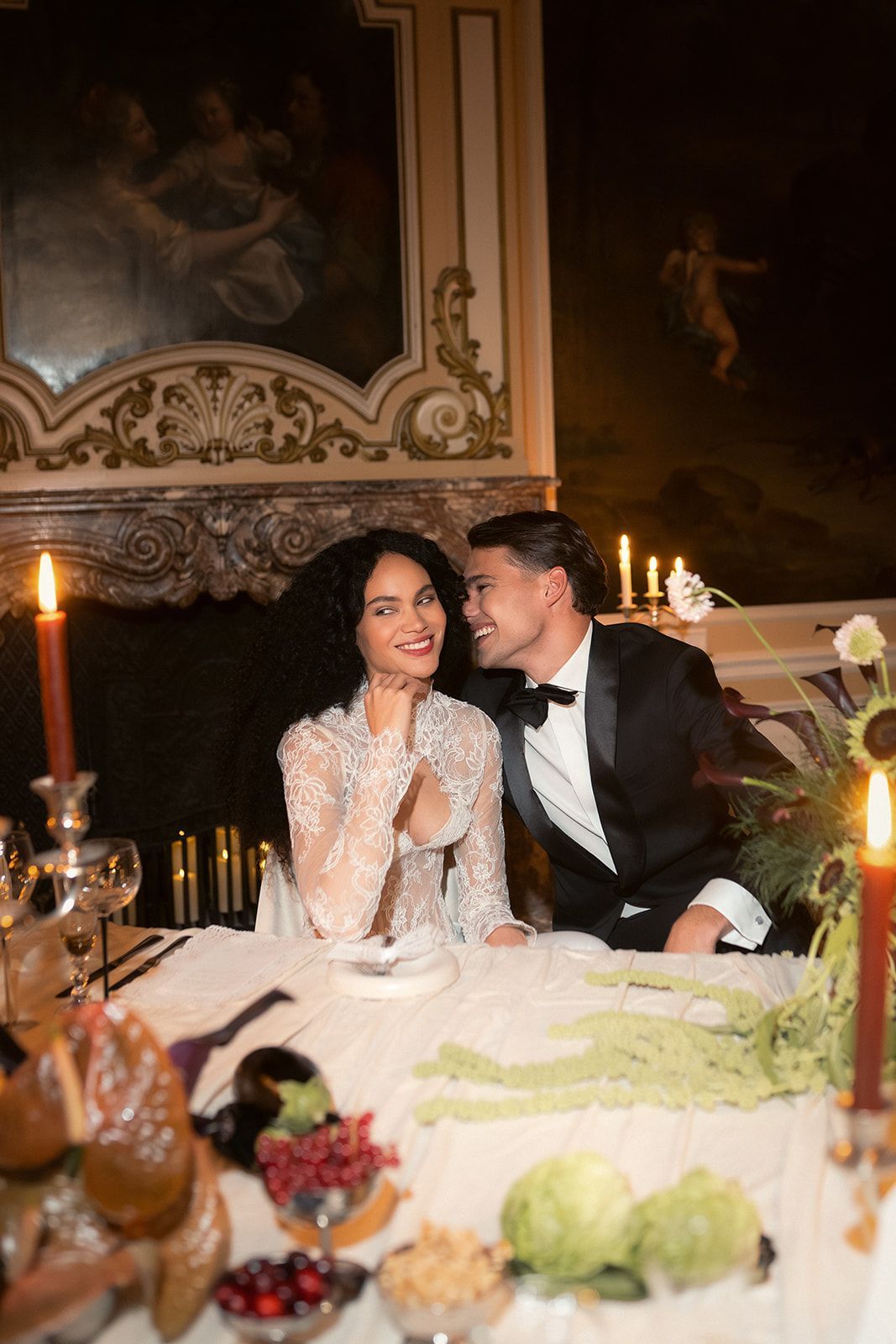 Couple in formal attire seated at a candlelit dinner table, smiling closely in an elegant dining room.