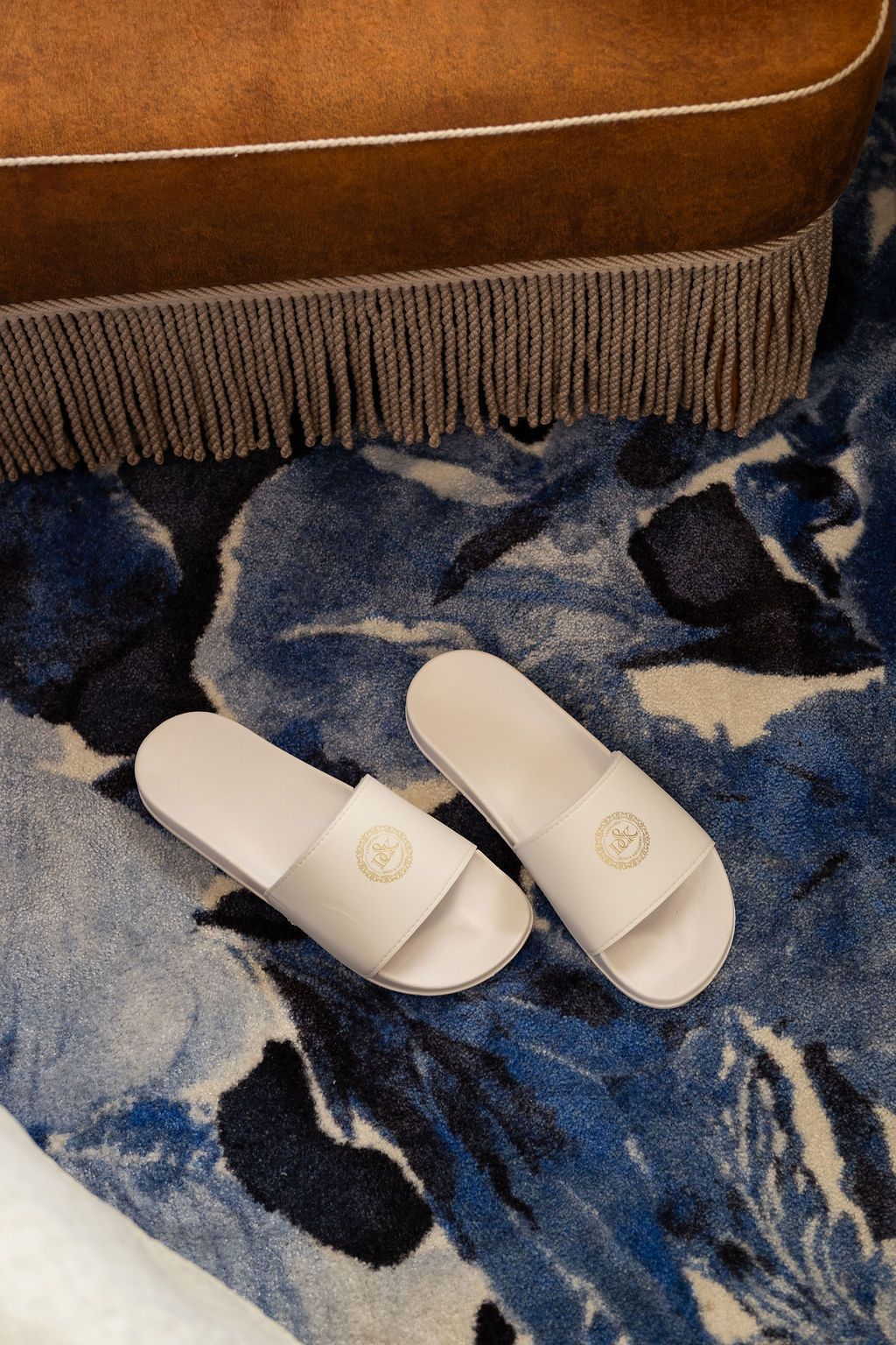 Witte slippers op een blauw patroonkleed naast een bruine stoel met franjes.