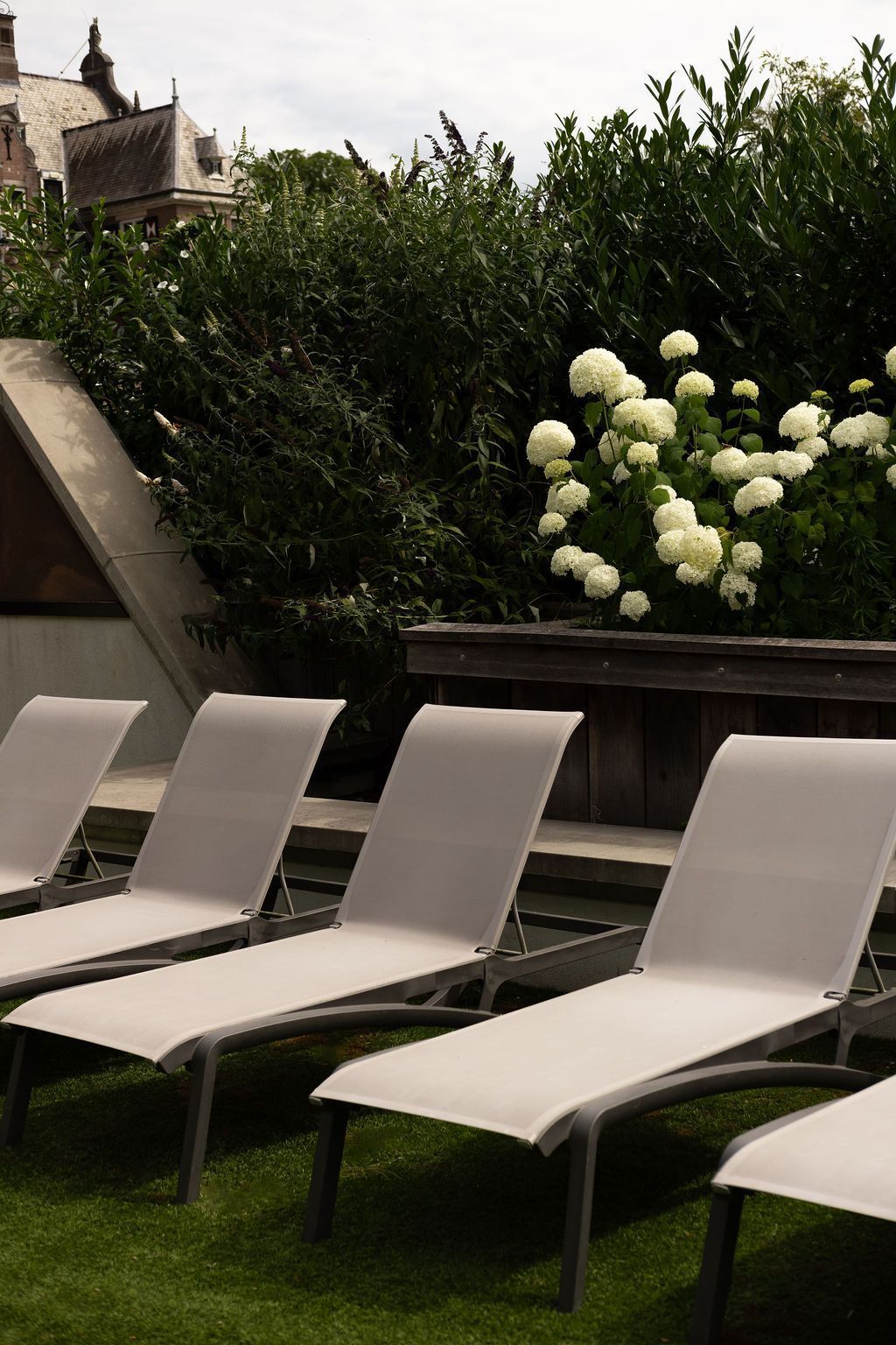 Witte loungestoelen in een tuin naast donkere hagen en witte bloemen.