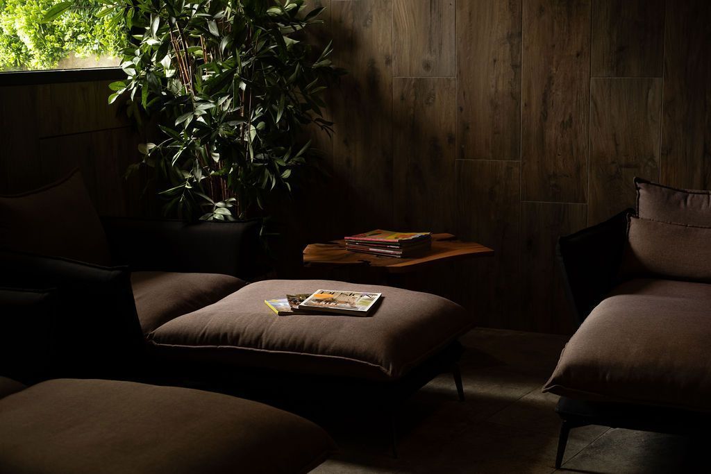 Een schemerige lounge met comfortabele stoelen, een lage tafel en een potplant tegen een muur met structuurverf.