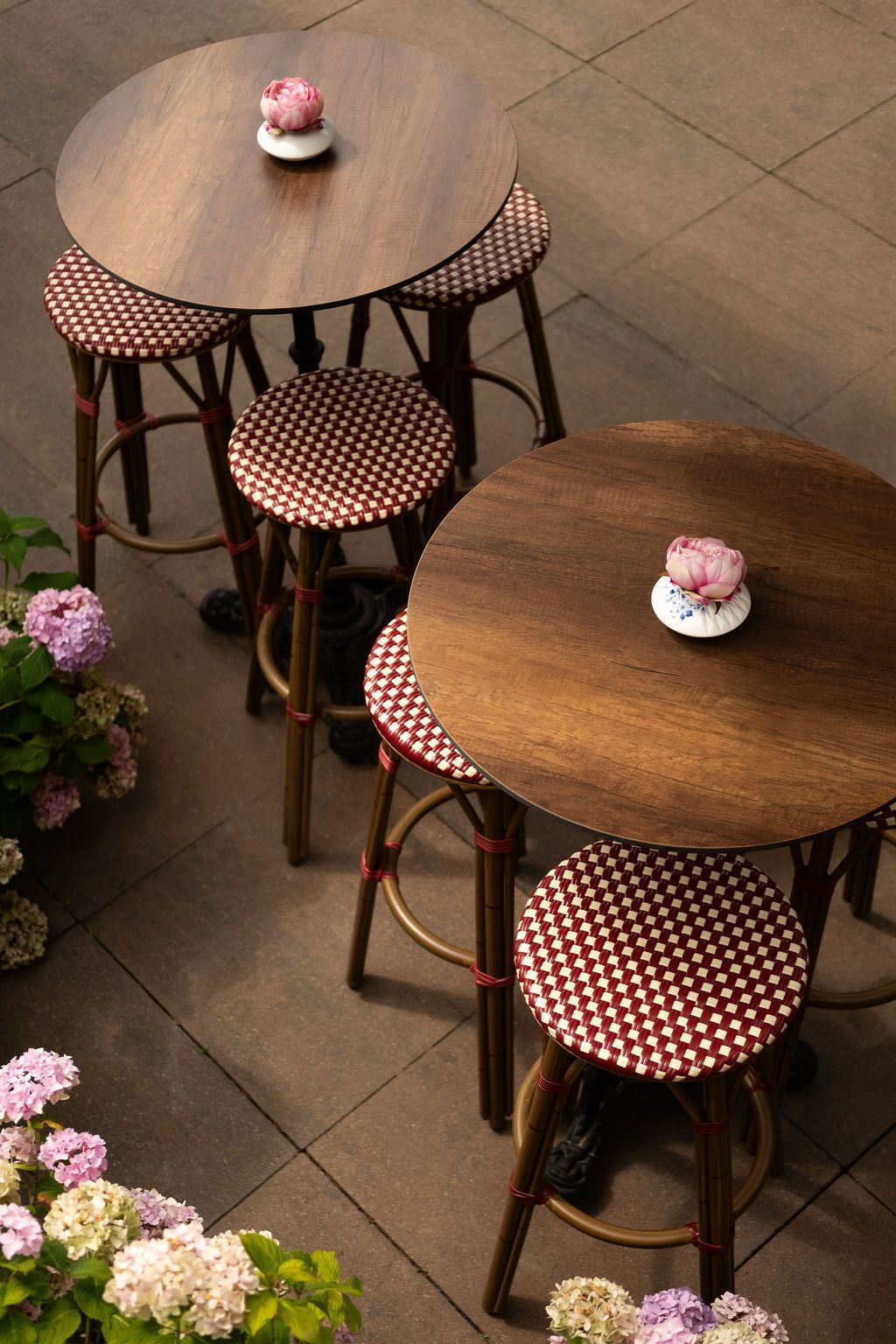 Twee kleine cafétafels met krukjes op een betegeld terras, elk versierd met een cupcake in het midden.