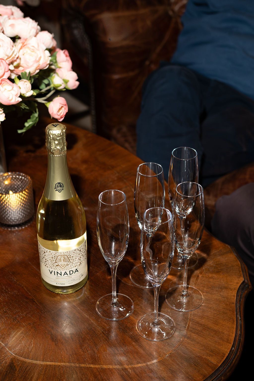 Een fles champagne en lege champagneglazen staan ​​op een houten tafel naast bloemen en een brandende kaars.