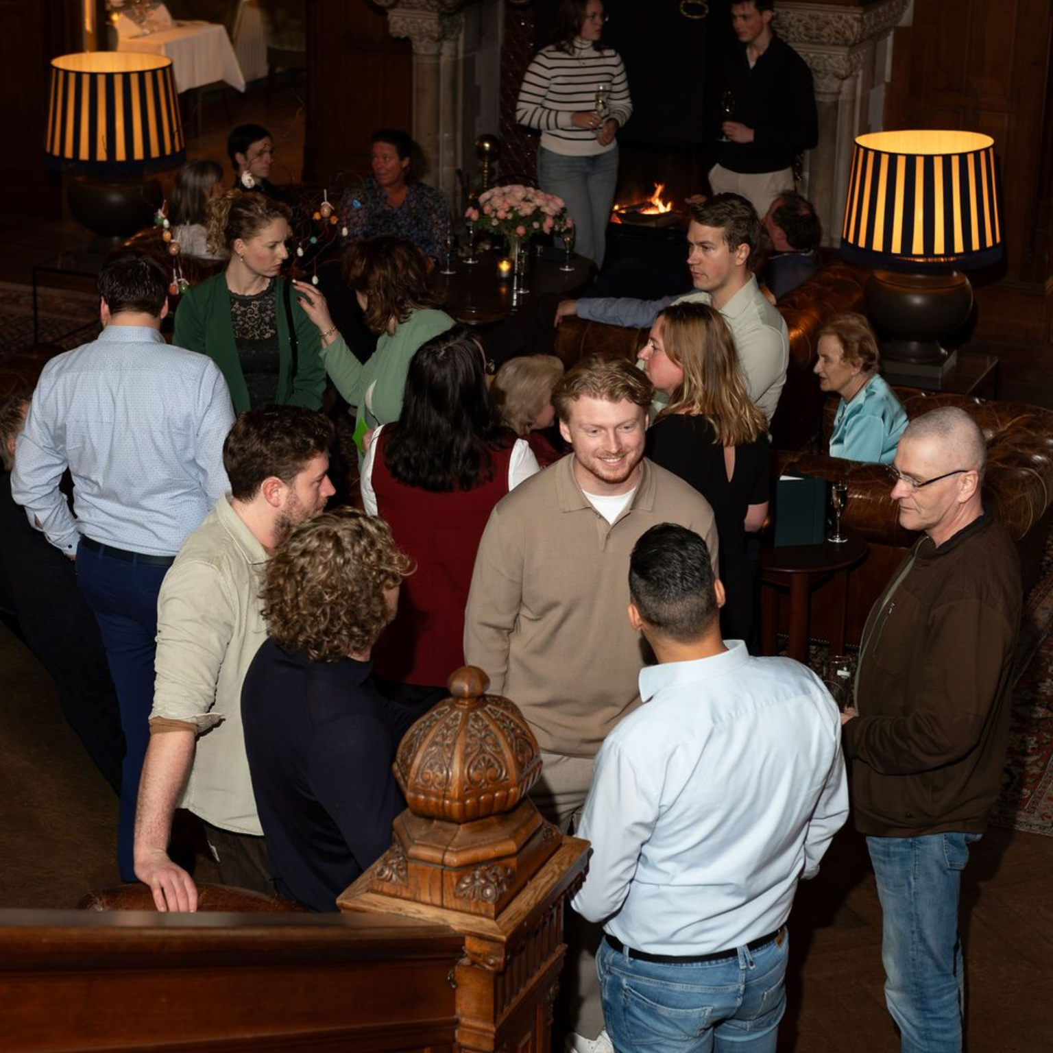 People chatting in a dimly lit lounge with dark wood decor and striped lamps.