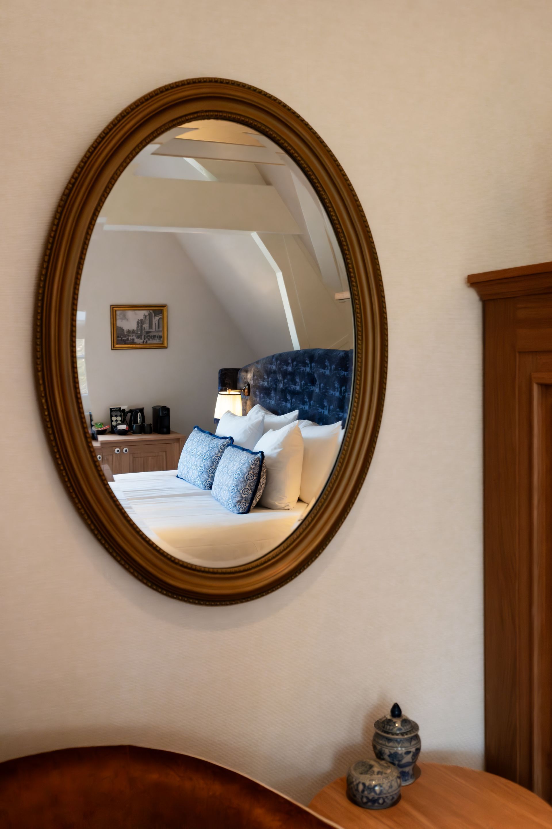 Oval mirror reflecting a bed with blue pillows in a cozy bedroom