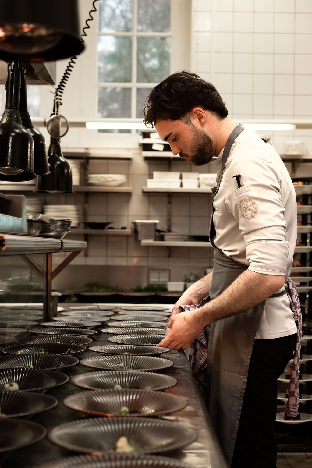 Chef arranging rows of plates in a tiled kitchen