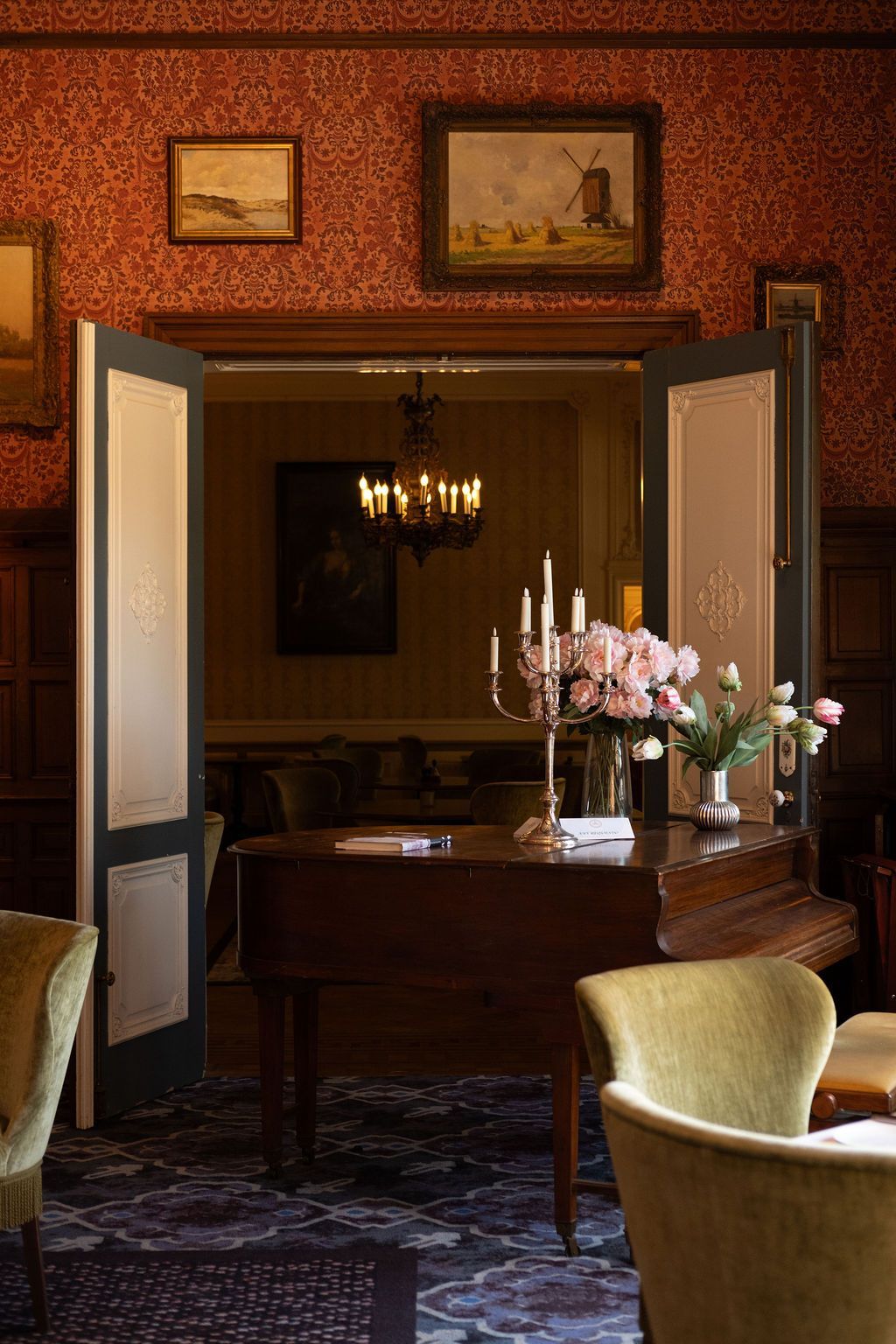 Elegante eetkamer met houten tafel, bloemstuk, kandelaars en ingelijste kunst aan roodkleurige muren met patroon.