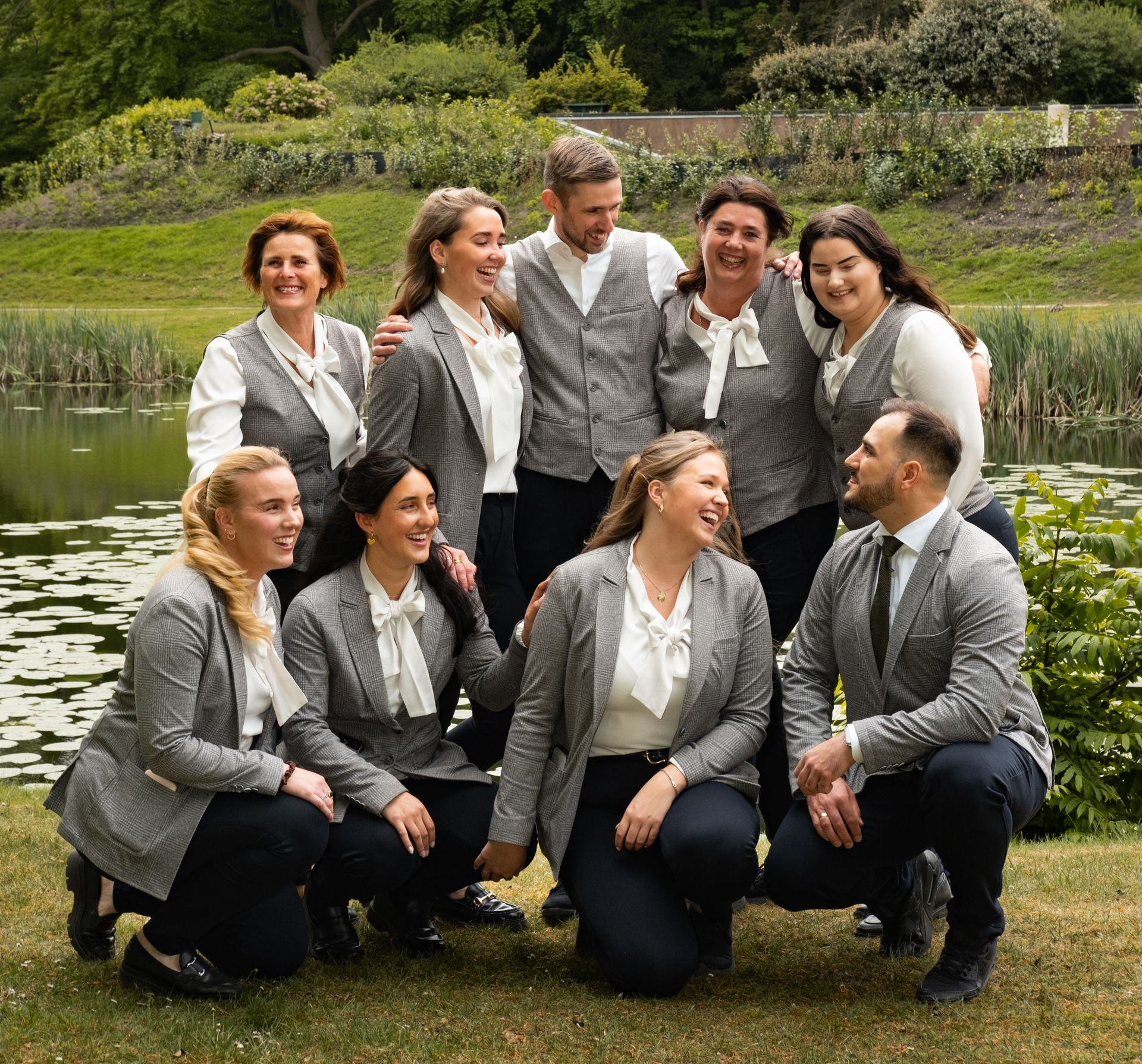 Vier personen in grijze blazers poseren binnen, drie staan ​​achter de persoon die ervoor zit.