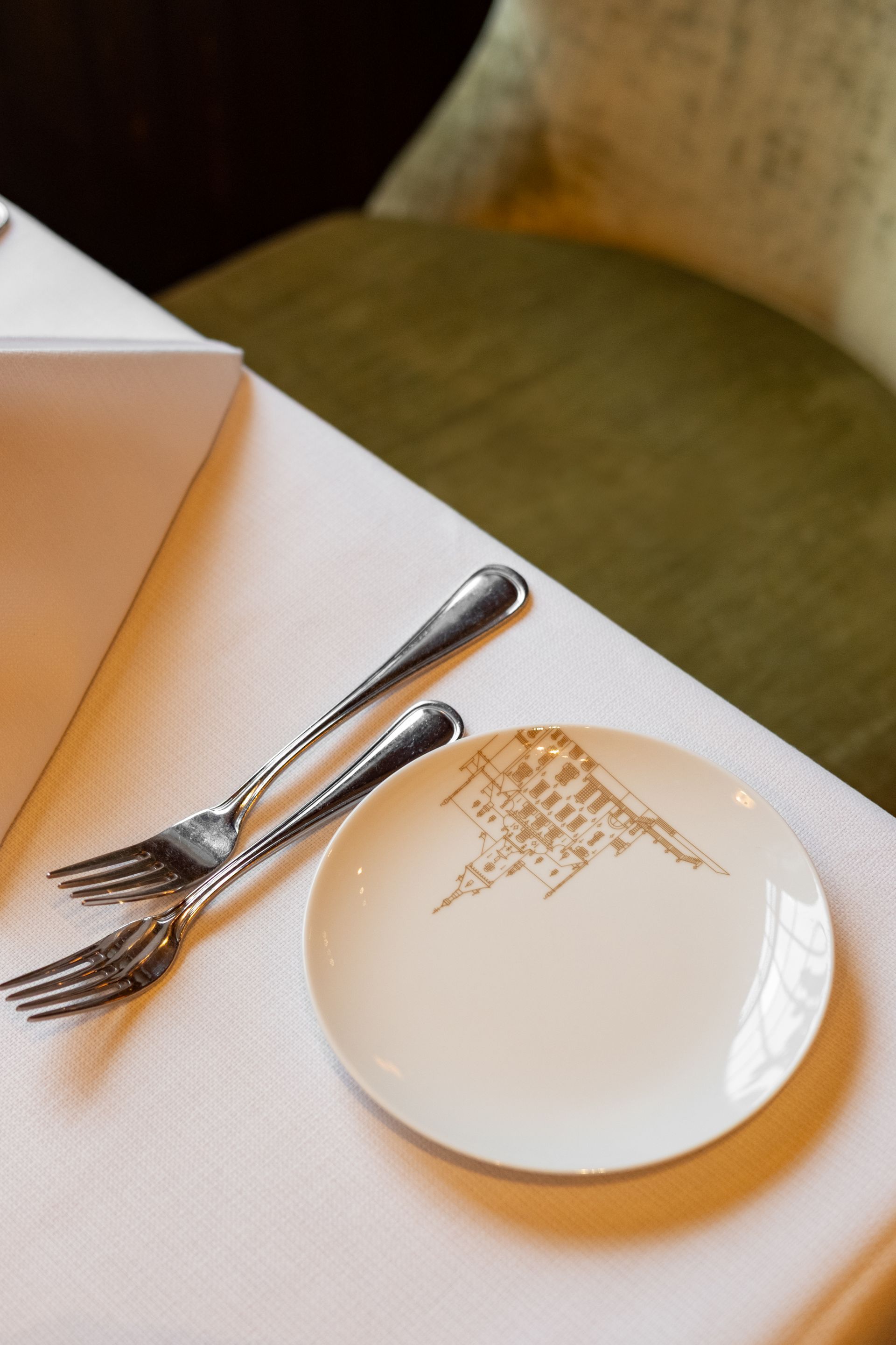 Silver fork and spoon on a white napkin beside a white plate on a table
