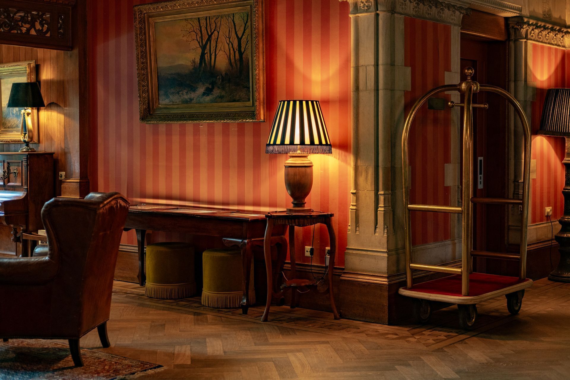 Elegante hotellobby met gestreept behang, lampen, banken en een bagagekar.