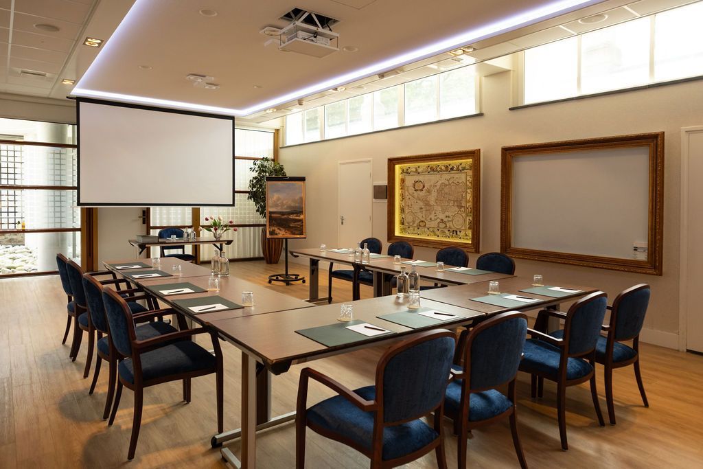 Vergaderruimte met een lange tafel, stoelen, projectiescherm en wanddecoratie in een warme verlichting.