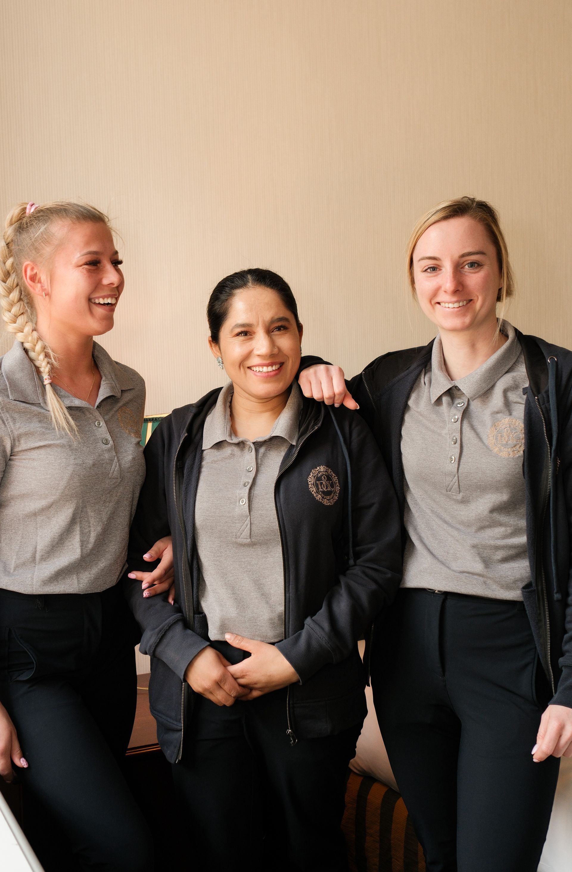 Three coworkers in gray polos and black jackets smiling and posing indoors