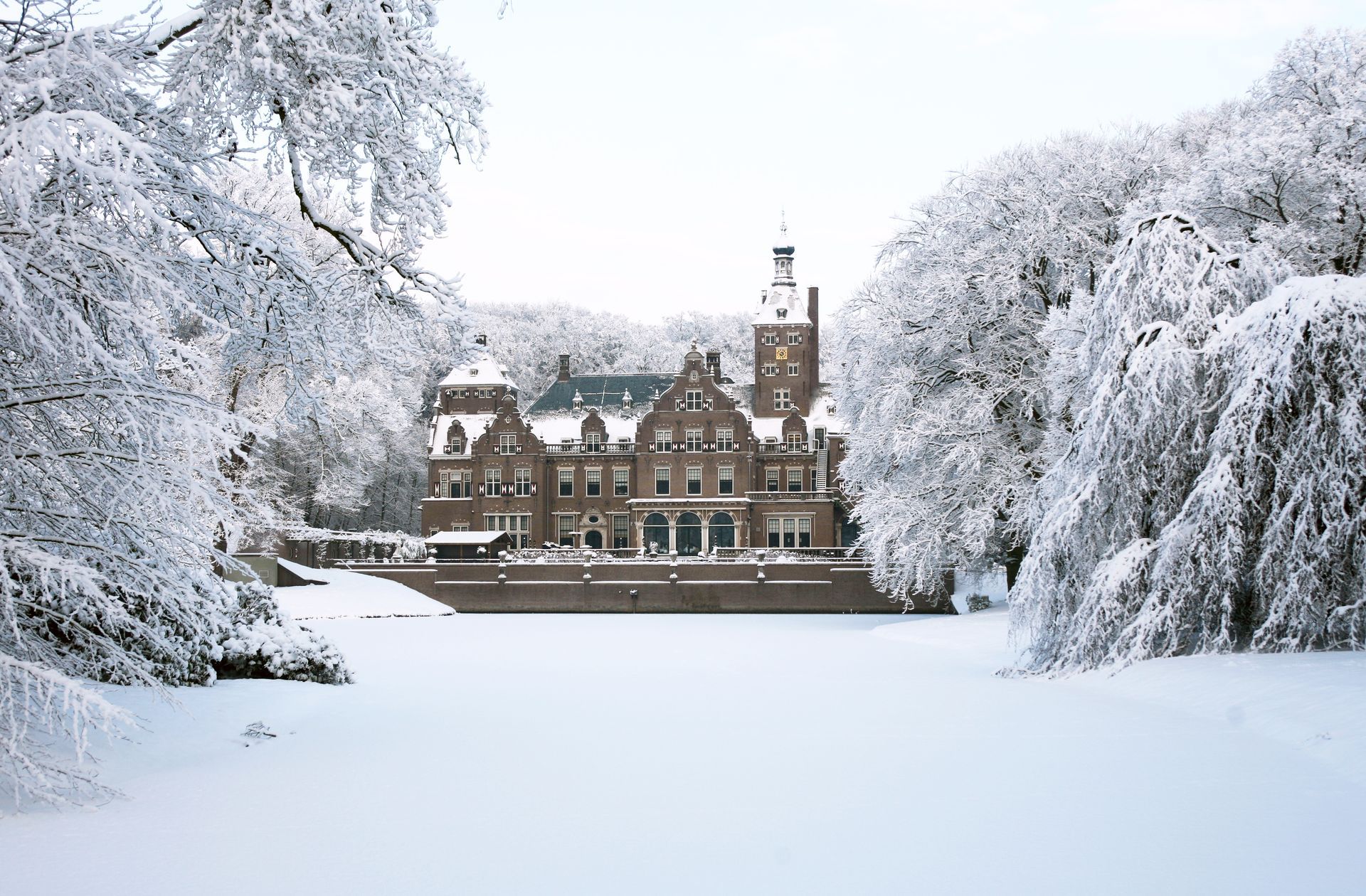Snow-covered mansion framed by frosted trees under a winter sky