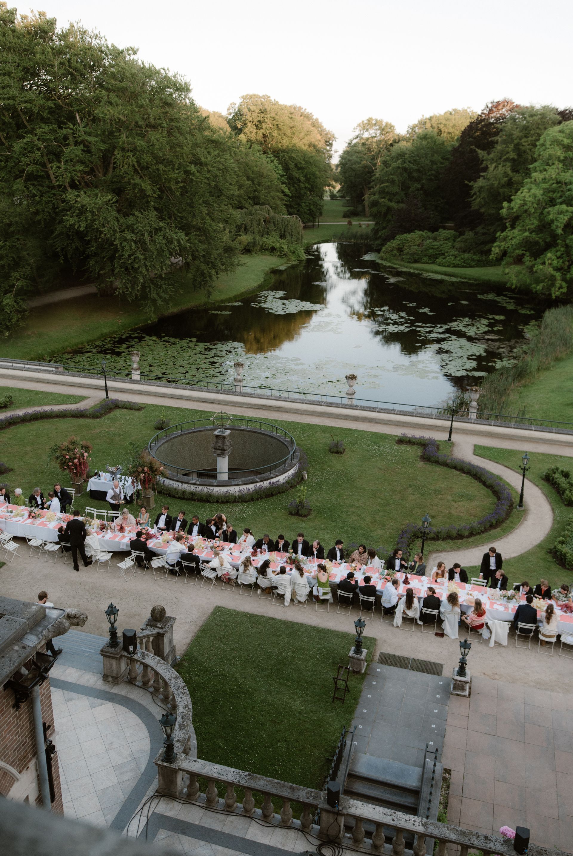 Crowd gathered along a canal and path in a green park at dusk