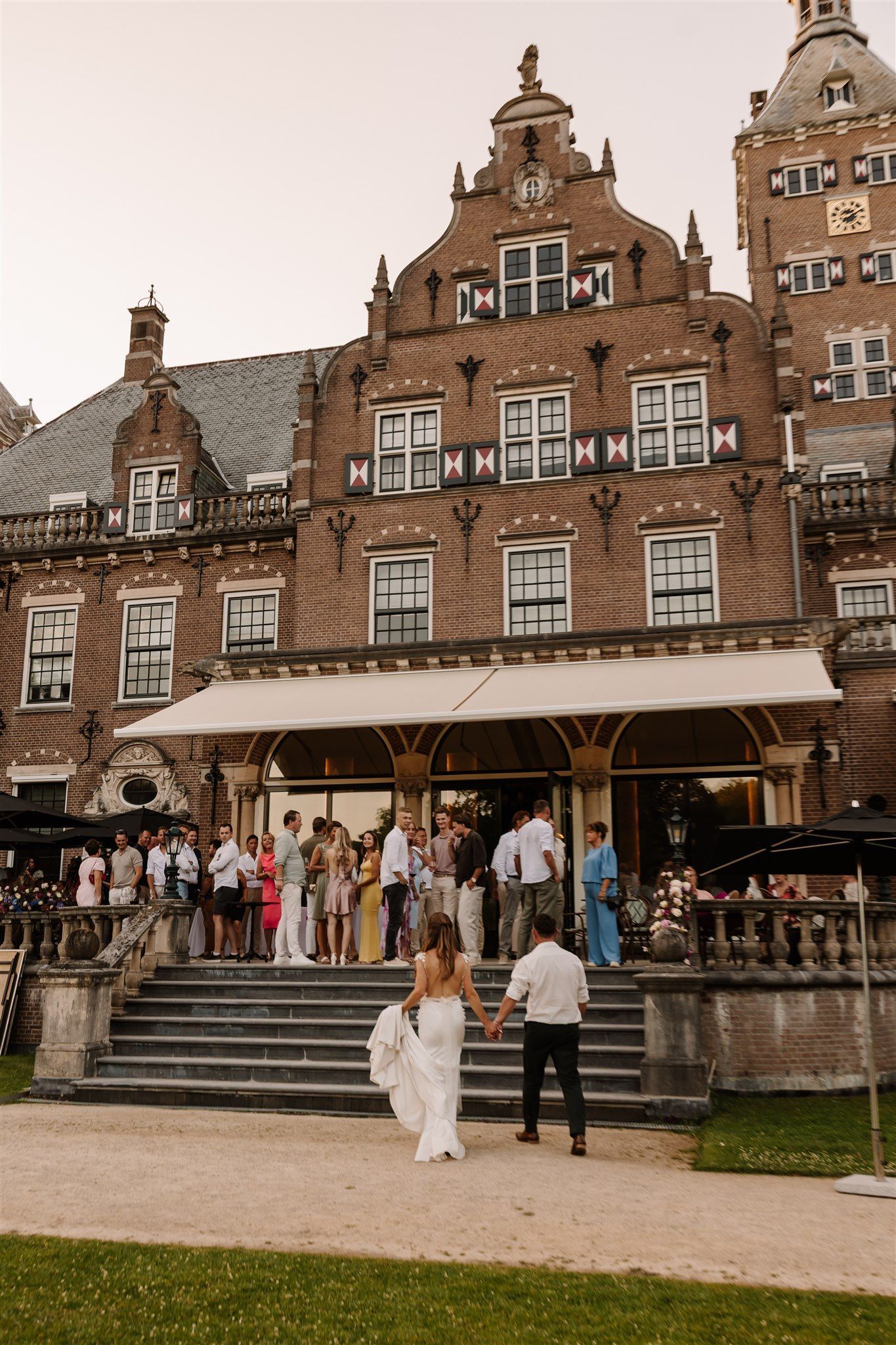 Historic brick building with a terrace café and people gathered outside, with a couple on the steps below