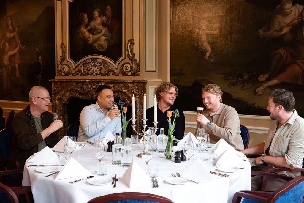 Five people seated at a dining table in a formal room, talking over drinks and water bottles