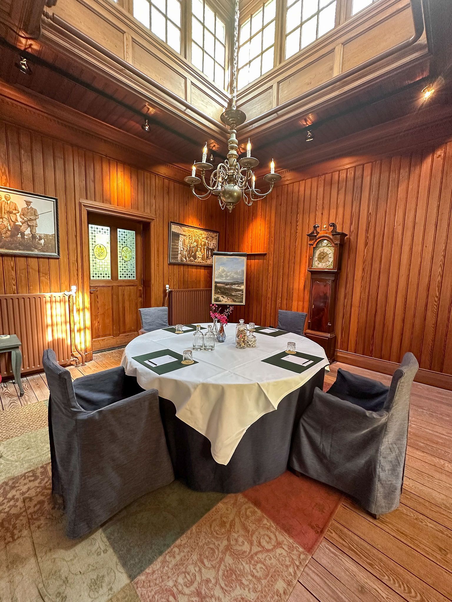 Elegant dining room with round table, six chairs, chandelier, and wood-paneled walls under a skylight