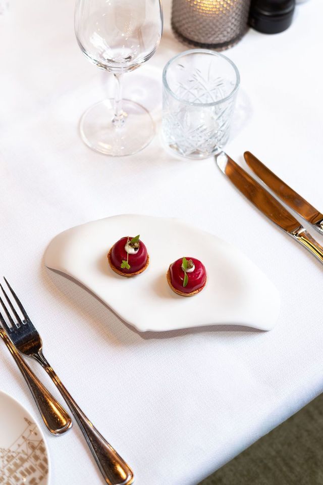 Elegant table setting with white cloth, gold cutlery, glasses, and two red garnishes on a white plate