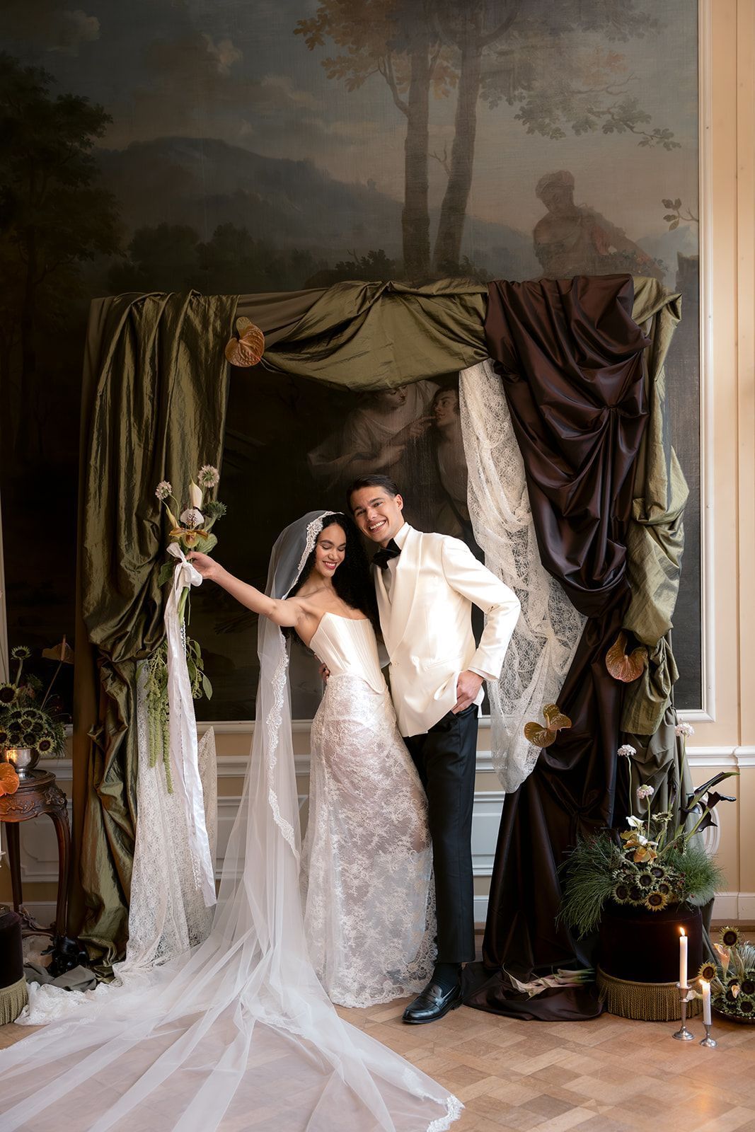 Wedding couple posing under a draped floral arch in a formal indoor setting