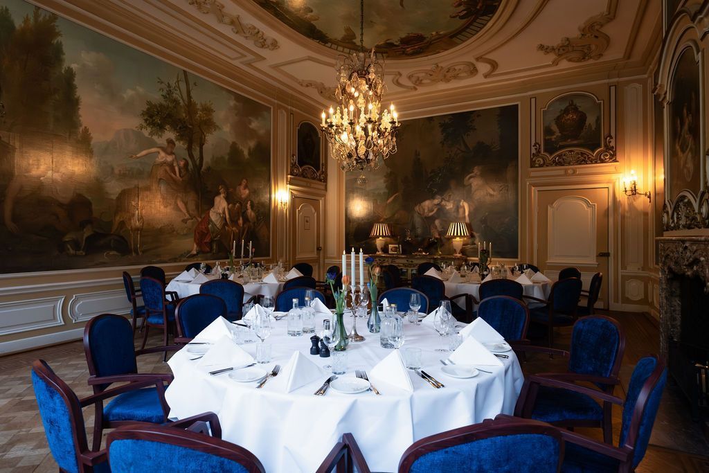 Elegant banquet hall with blue chairs, white-clothed tables, chandeliers, and painted walls