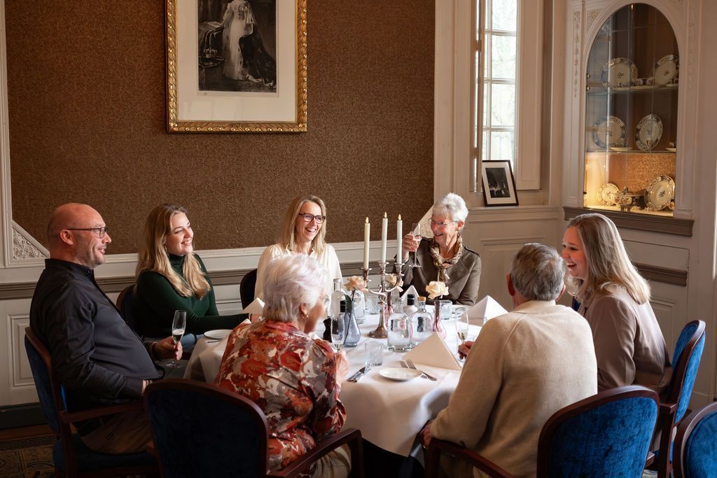 Group seated around a dining table in a warmly lit room with candles and bottles, engaged in conversation