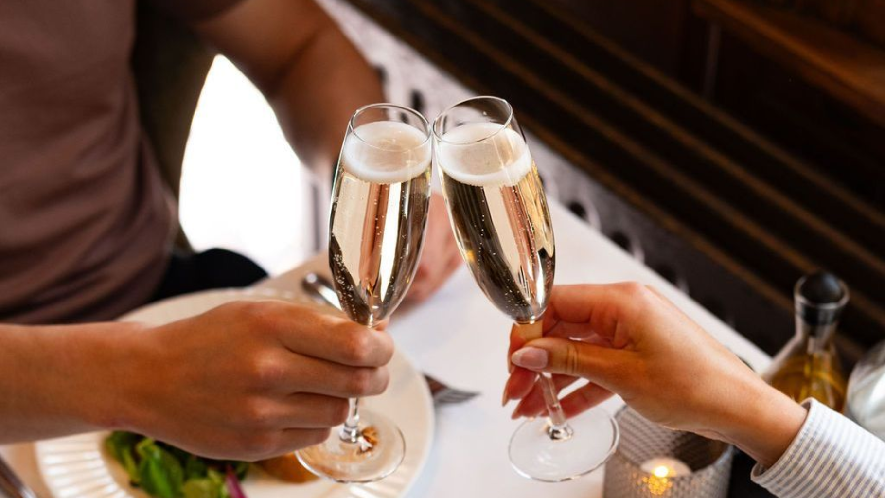 Twee mensen klinken hun champagneglazen tegen elkaar aan een tafel in een sfeervol verlicht restaurant.