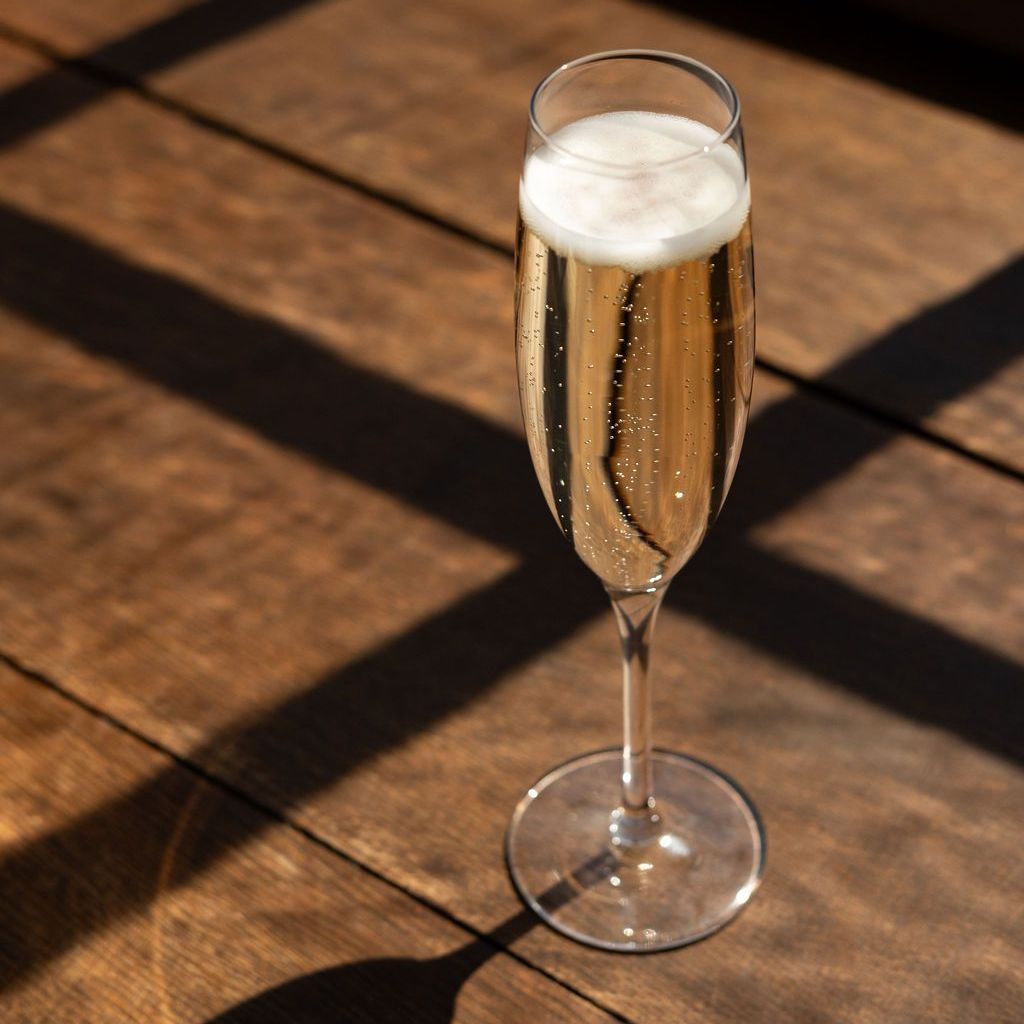 Een glas mousserende witte wijn op een zonnige houten tafel.