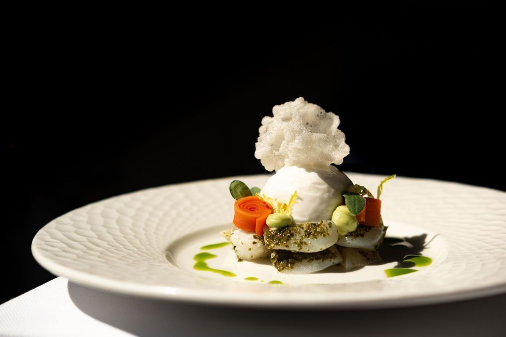 Elegant opgemaakt dessert met witte sorbet, groene garnering en kleurrijk fruit op een wit bord.